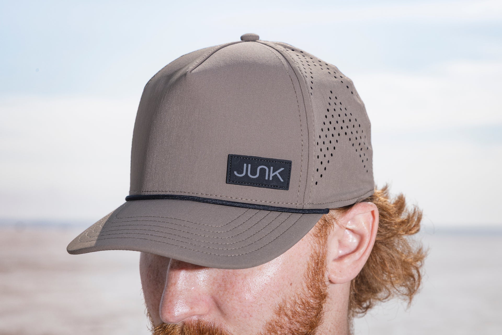 Man wearing an Apex hat in Morel color with 'JUNK' logo on a beach.