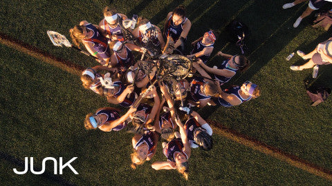 many women on the lacrosse team holding their sticks together, JUNK logo in bottom left corner