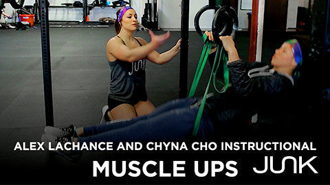 woman coaching another person, both wearing junk headbands on the fundamentals of muscle ups