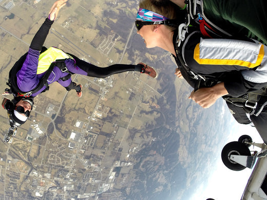 woman at fun angle and other woman smiling at her as they jump from an airplane to skydive