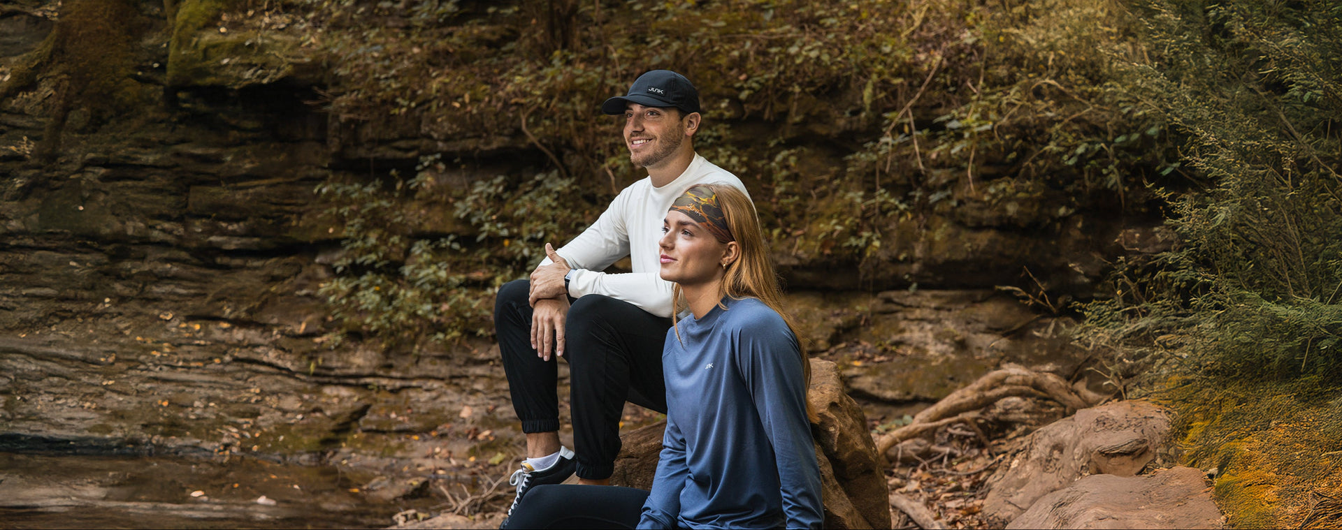 Two people sitting on a rock by a river with a forest background
