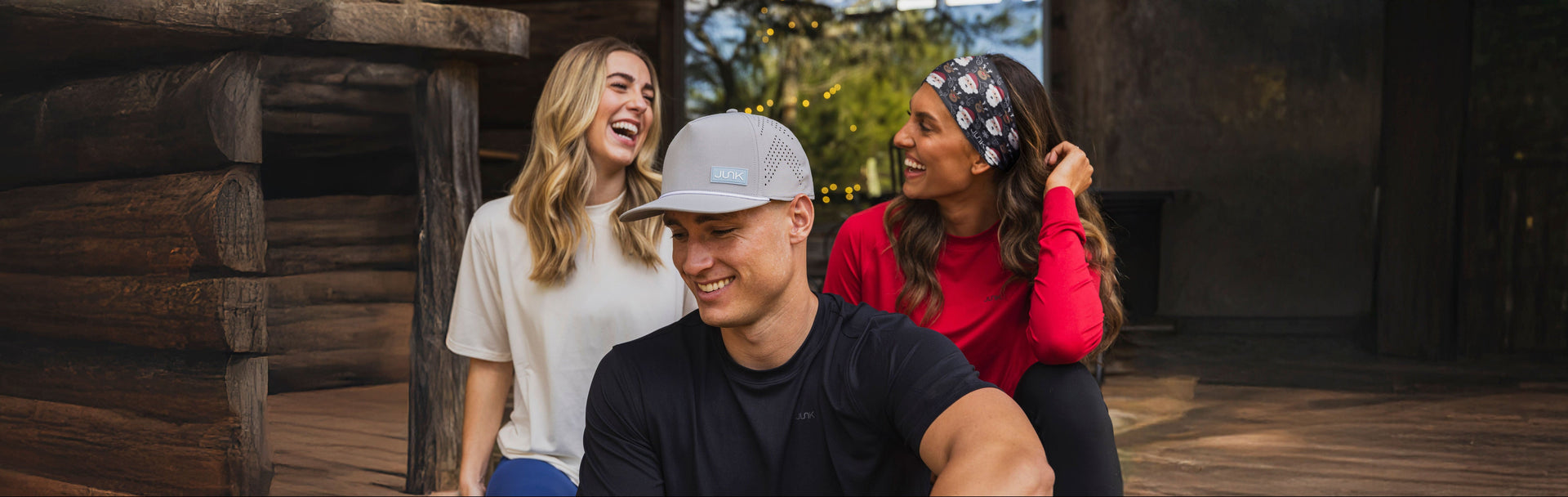 Three people sitting near a wooden structure outdoors wearing JUNK gear.