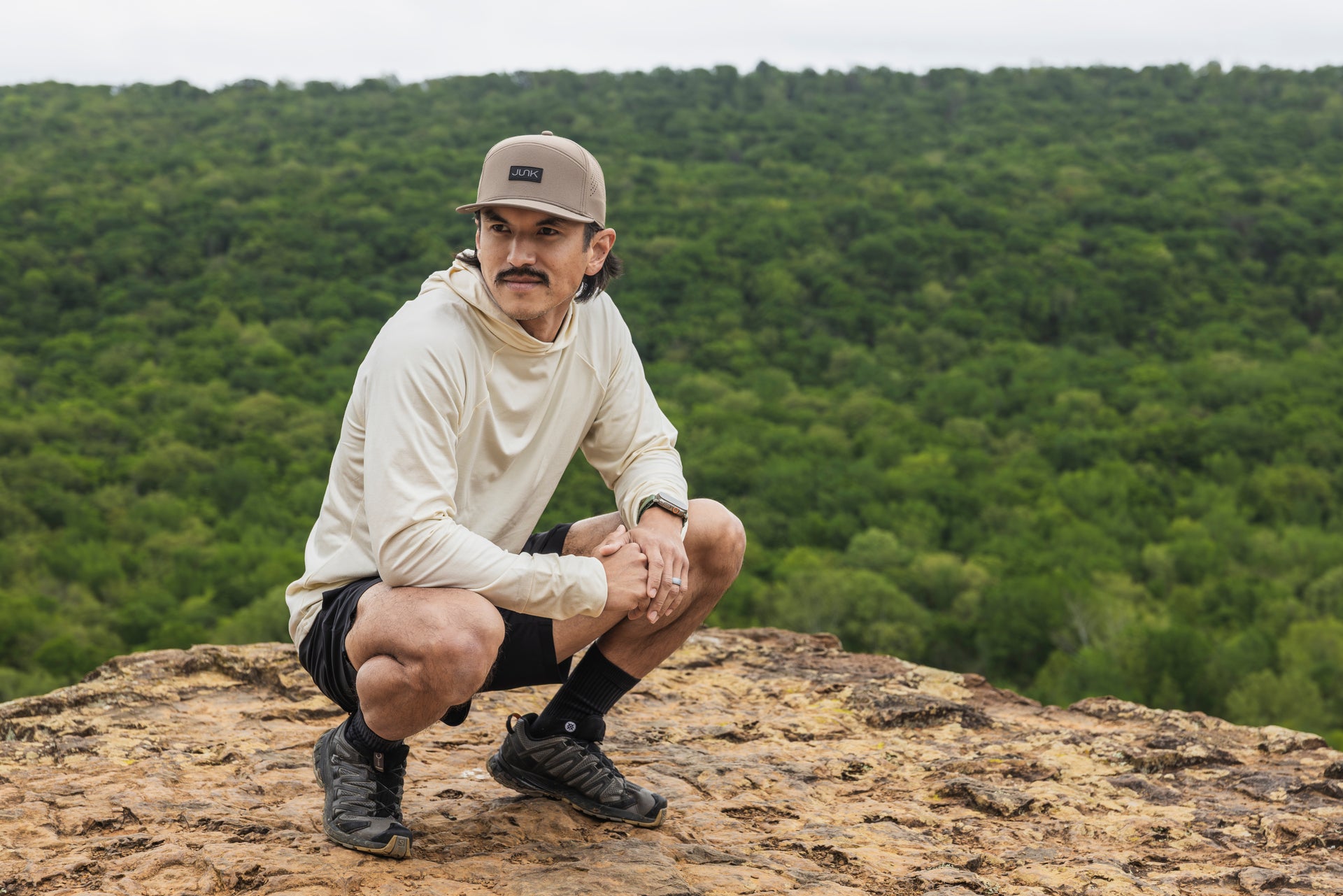 Man crouching on a rocky outcrop with a forest in the background