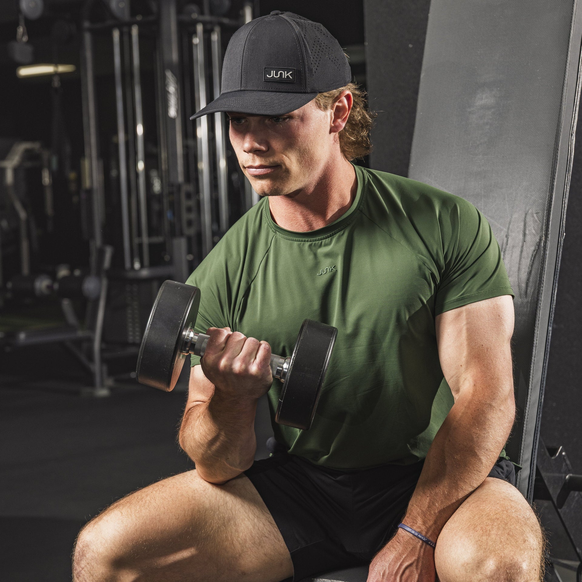 Man in green shirt and black cap lifting weights in a gym.