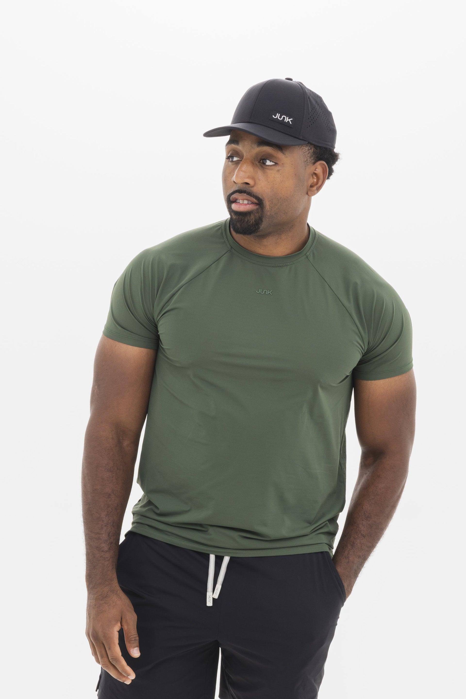 Man wearing a green t-shirt, black shorts, and a cap on a white background