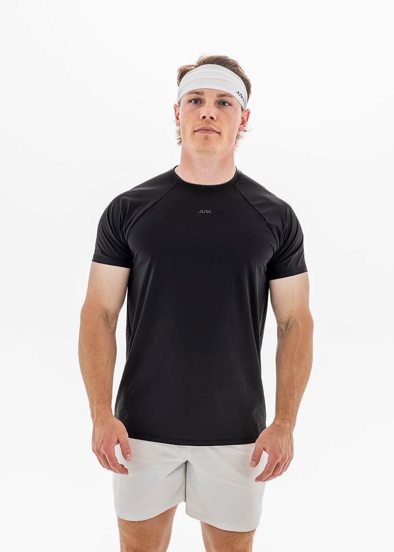 A man wearing a black short-sleeve athletic t-shirt with a small white logo on the chest, paired with white shorts and a white headband, photographed against a clean white background.